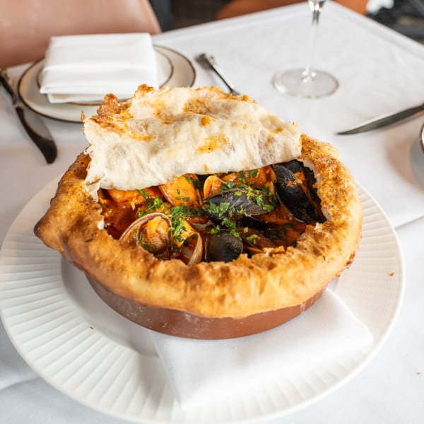 A baked seafood dish with mussels and clams in a terracotta pot, topped with a golden crust.