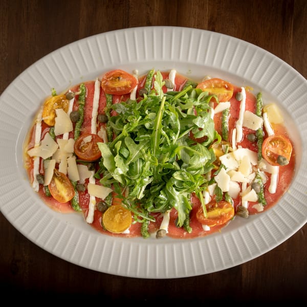 Italian carpaccio with arugula, cherry tomatoes, capers, and parmesan cheese on a white platter.