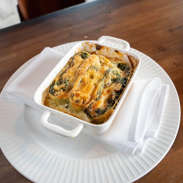 A white baking dish of baked Italian cannelloni with melted cheese, on a white plate with a napkin.