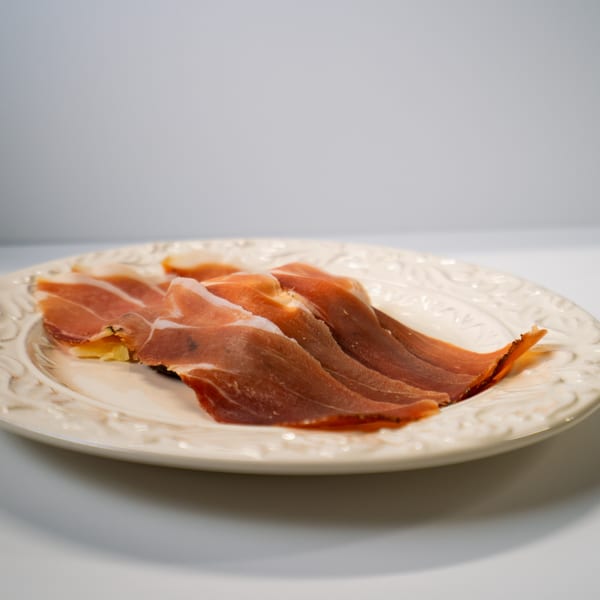 Thinly sliced Italian prosciutto, with delicate marbling, arranged on a decorative white plate.