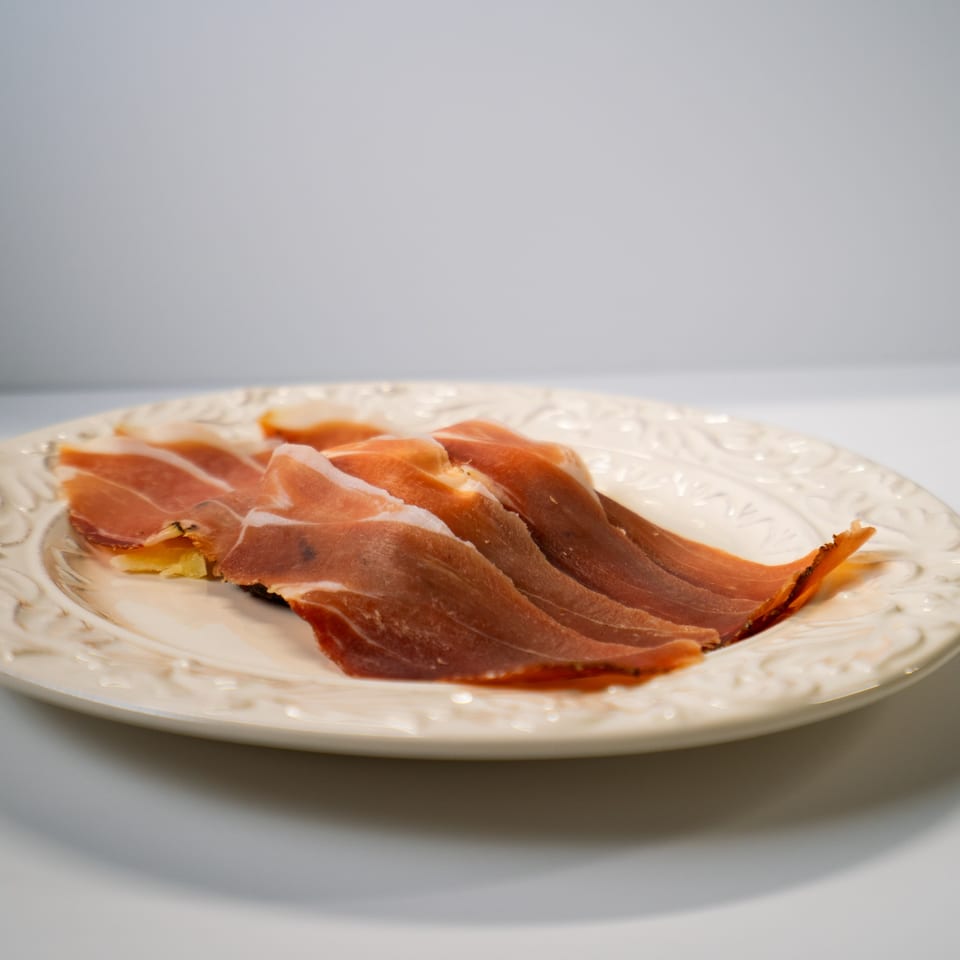 Thinly sliced Italian prosciutto, with delicate marbling, arranged on a decorative white plate.