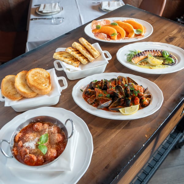 A wooden table laden with various Italian dishes, including mussels, meatballs, and grilled bread.
