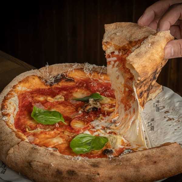 A hand pulls a slice of Sicilia Mia pizza, stretching melted cheese from the pie.
