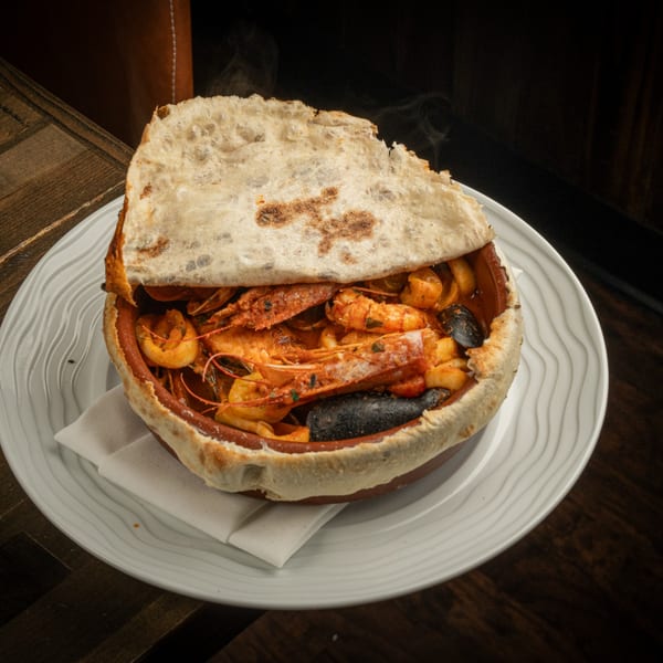 Steaming hot seafood stew with prawns, mussels, and squid, topped with a baked flatbread crust.