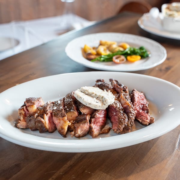 Sliced steak with herb butter on a white plate, with a side dish of vegetables in the background.