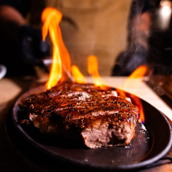 Flambéed steak on a sizzling cast iron plate, with bright orange flames rising from the dish.