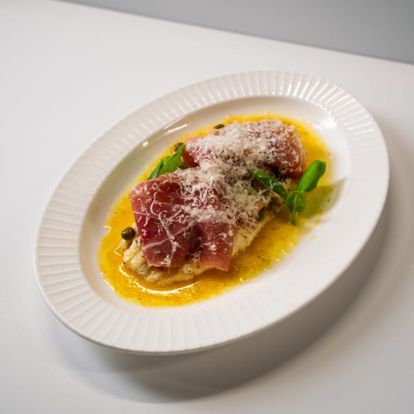 Italian dish with prosciutto, parmesan, and basil in a yellow sauce on a white oval plate.